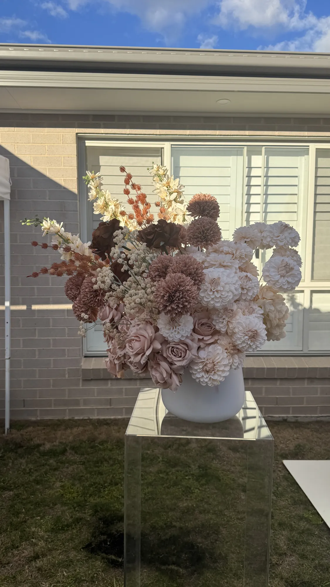 A floral arrangement of white, pink, and blue flowers with greenery on a clear acrylic plinth.