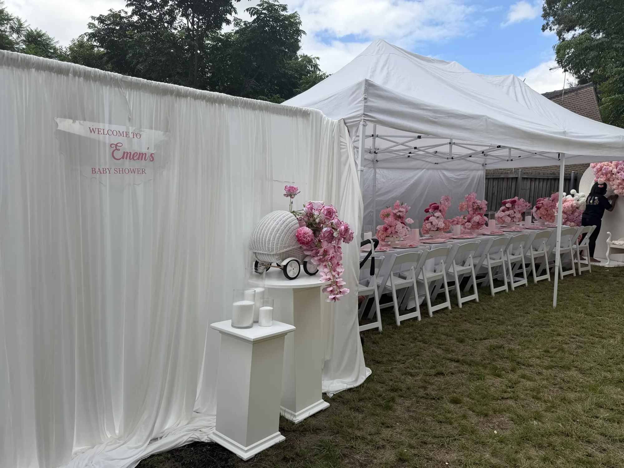 A low white floral centrepiece on a round table in white linen, with white napkins, gold cutlery, and a menu card.