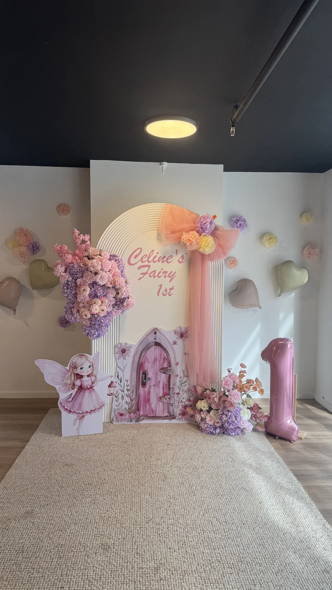 A butterfly cake on a glass stand in front of a fairy backdrop, with butterfly wings and a marquee 1.