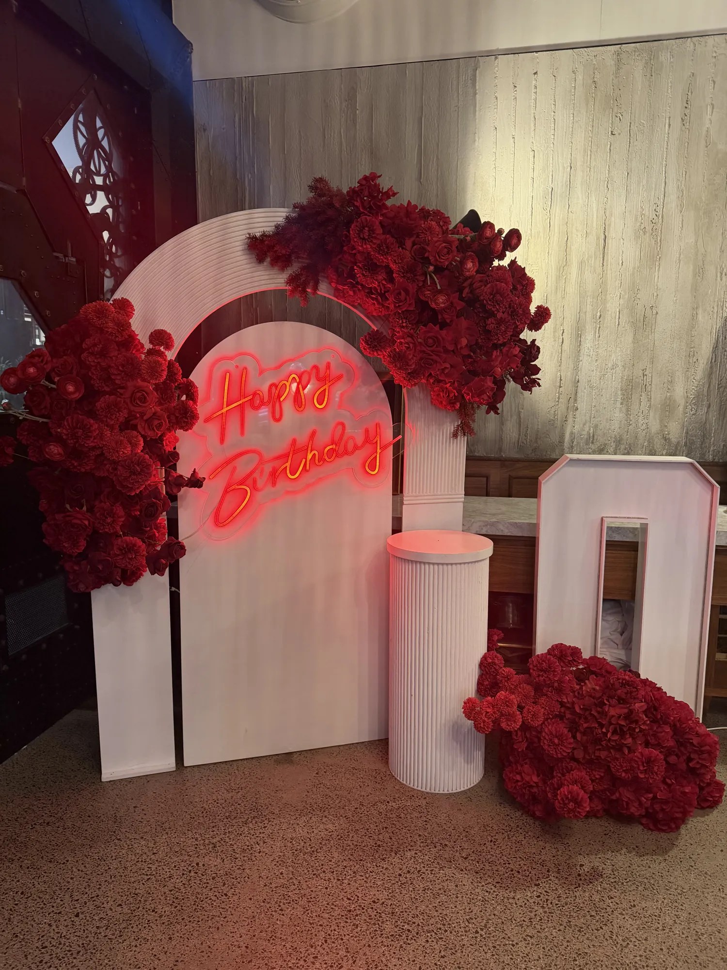 A long table in white linen with red napkins and a red rose runner, with a marquee 30 and a white arch at the far end.