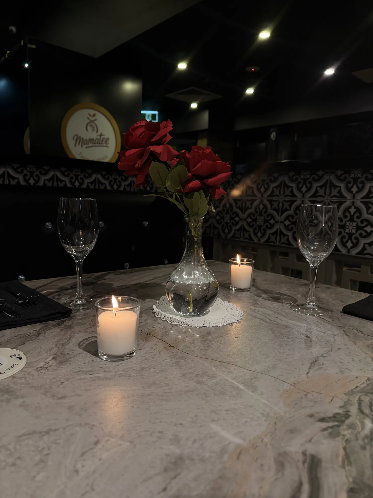A white backdrop with a pink neon sign reading Mamatee, white flowers, and clear plinths holding small dishes.