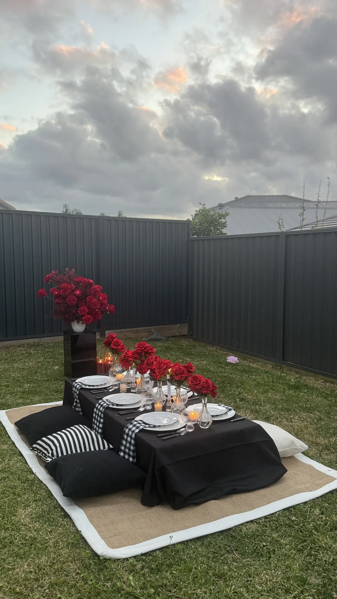 A place setting on a picnic table, with a white napkin, gold cutlery, a glass, and a white floral centrepiece.