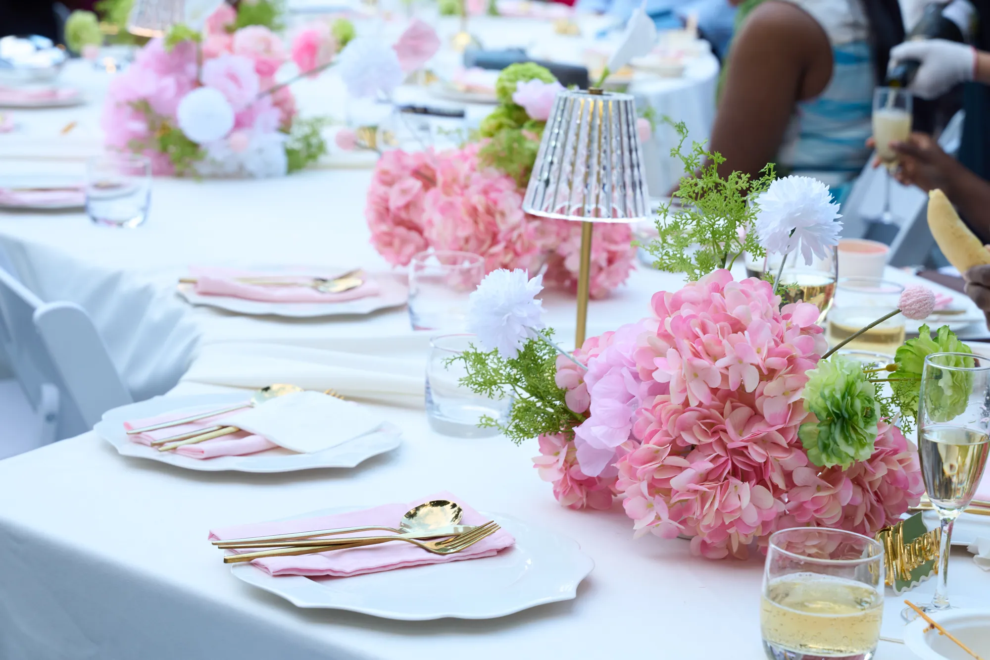 A place setting with a pink hydrangea, a pink napkin, gold cutlery, and a menu card.