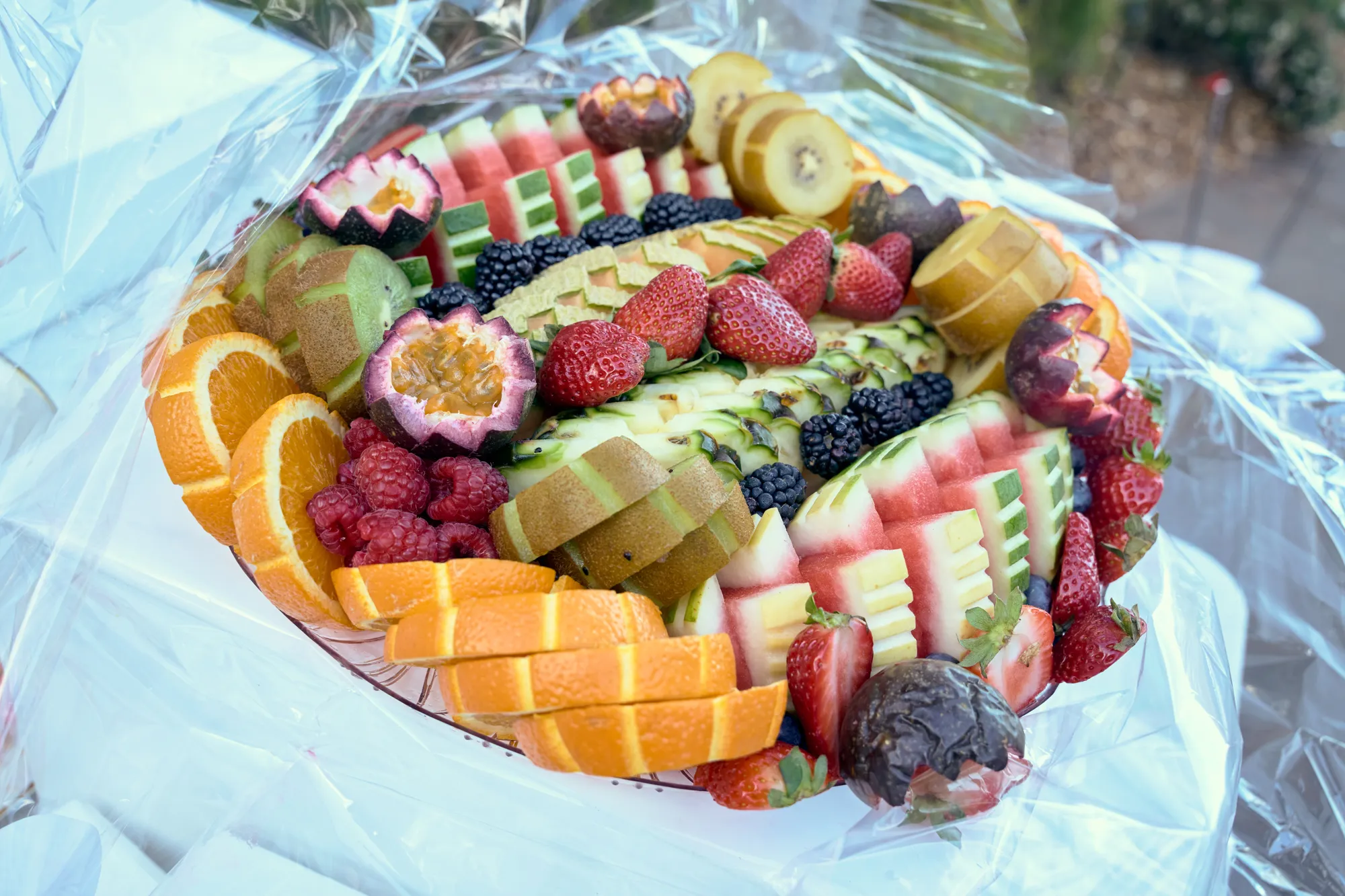 A fruit platter of pineapple, melon, strawberries, and grapes around a small vase of pink and white flowers.
