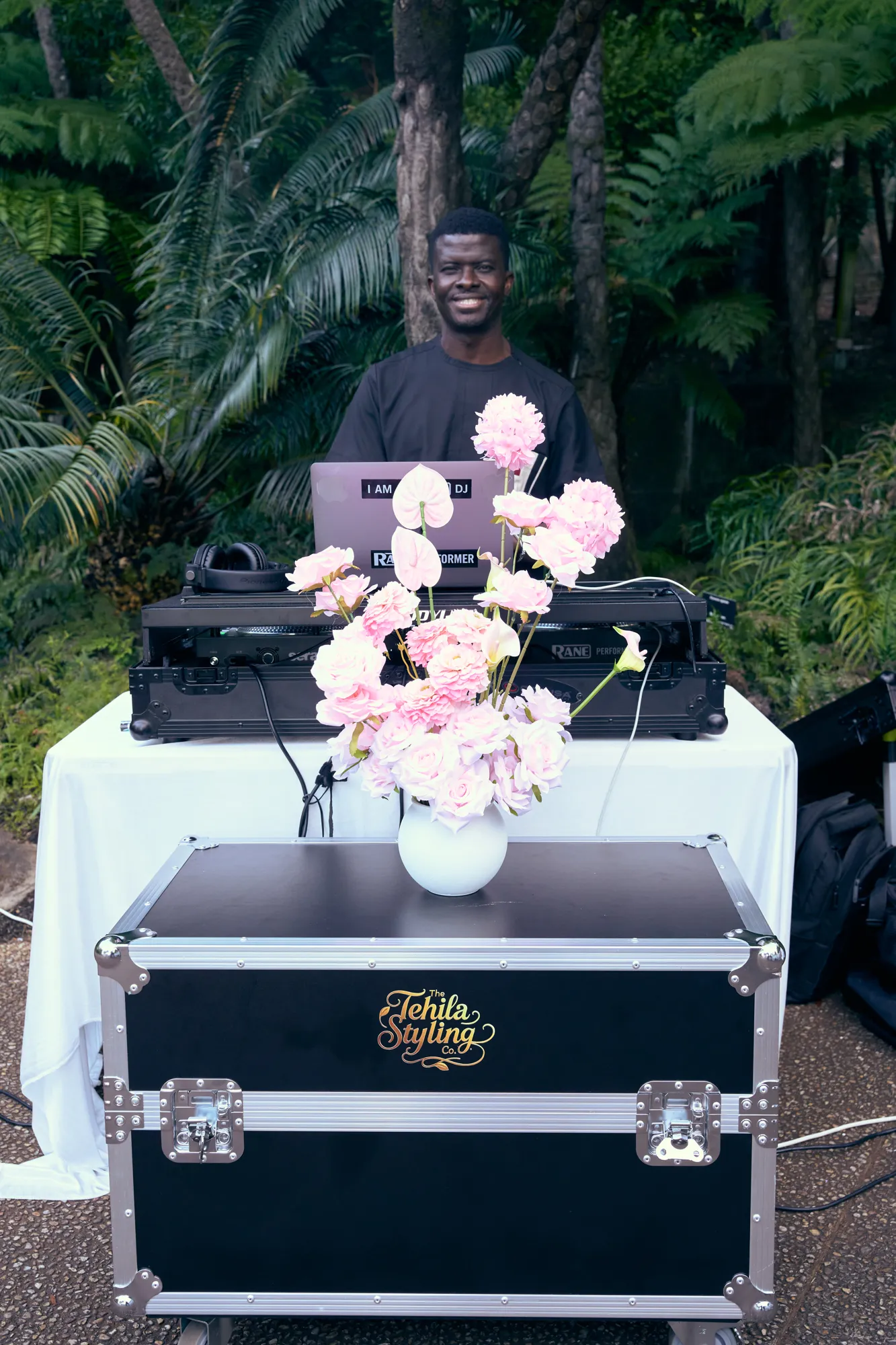 A white DJ booth decorated with white flowers and a pink neon sign, with a laptop open.