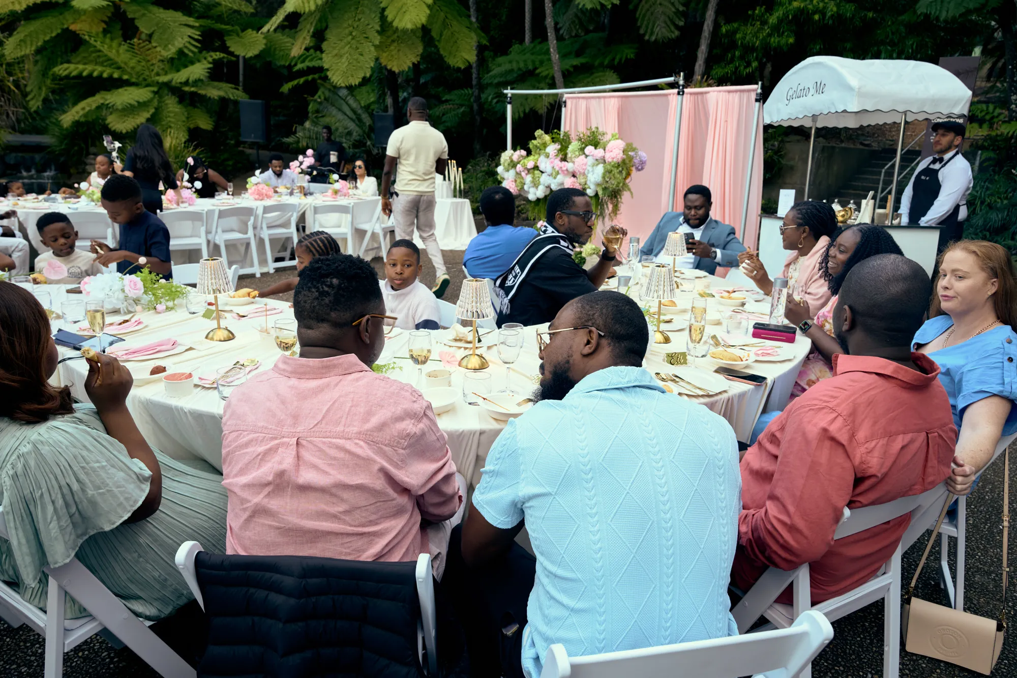 Guests seated along a white table with pink napkins and low floral arrangements.