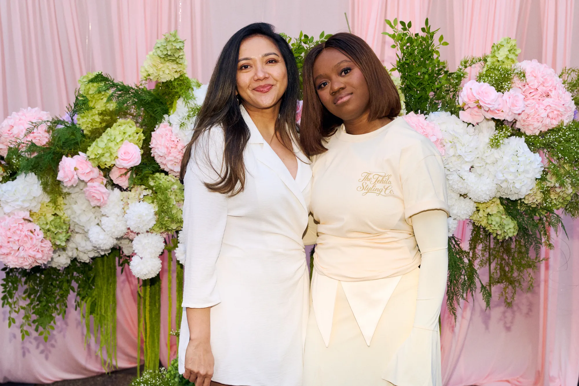 Two guests standing in front of a white floral backdrop and a pink neon sign.