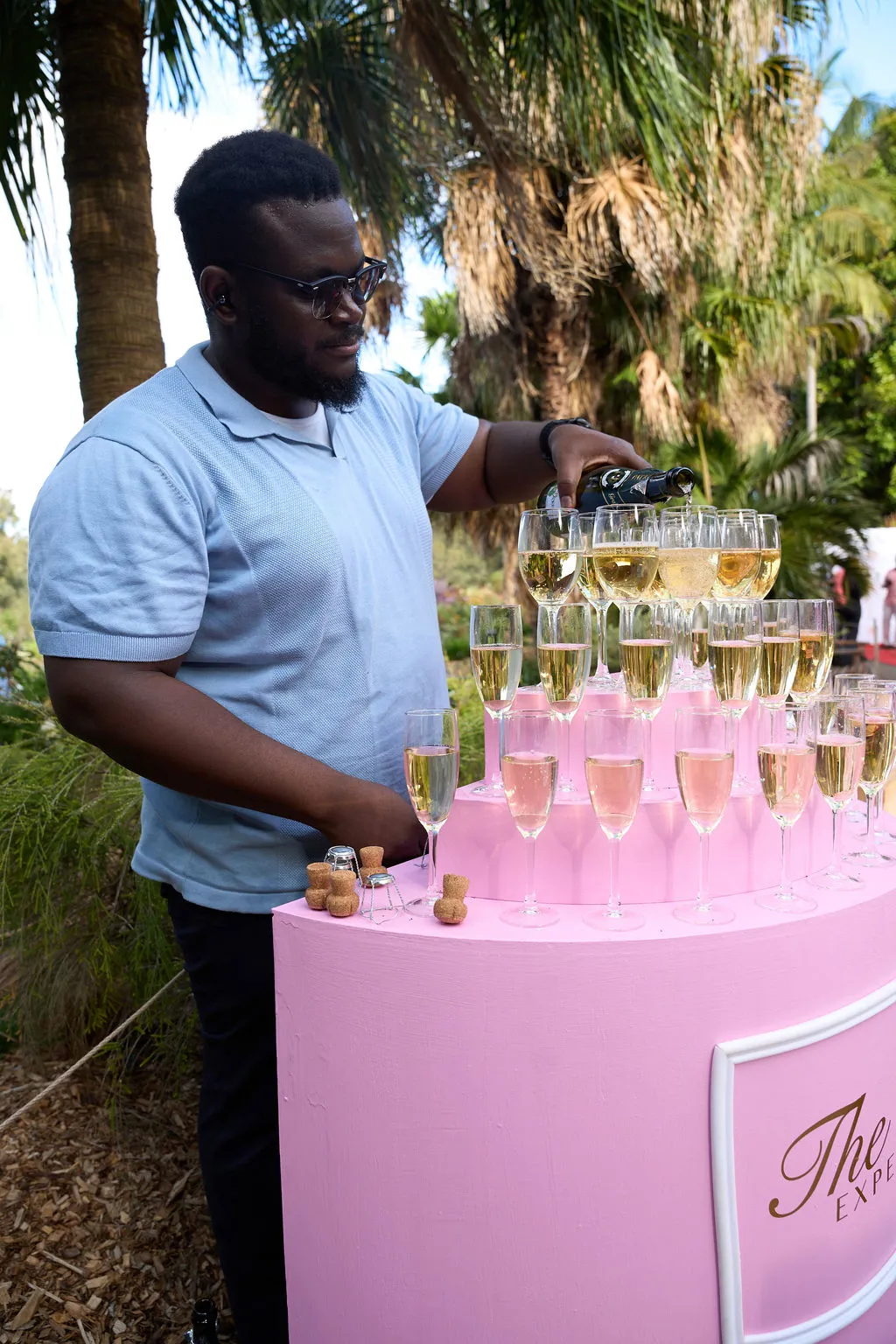 Champagne poured into a tower of flutes on a pink stand topped with pink and white flowers.