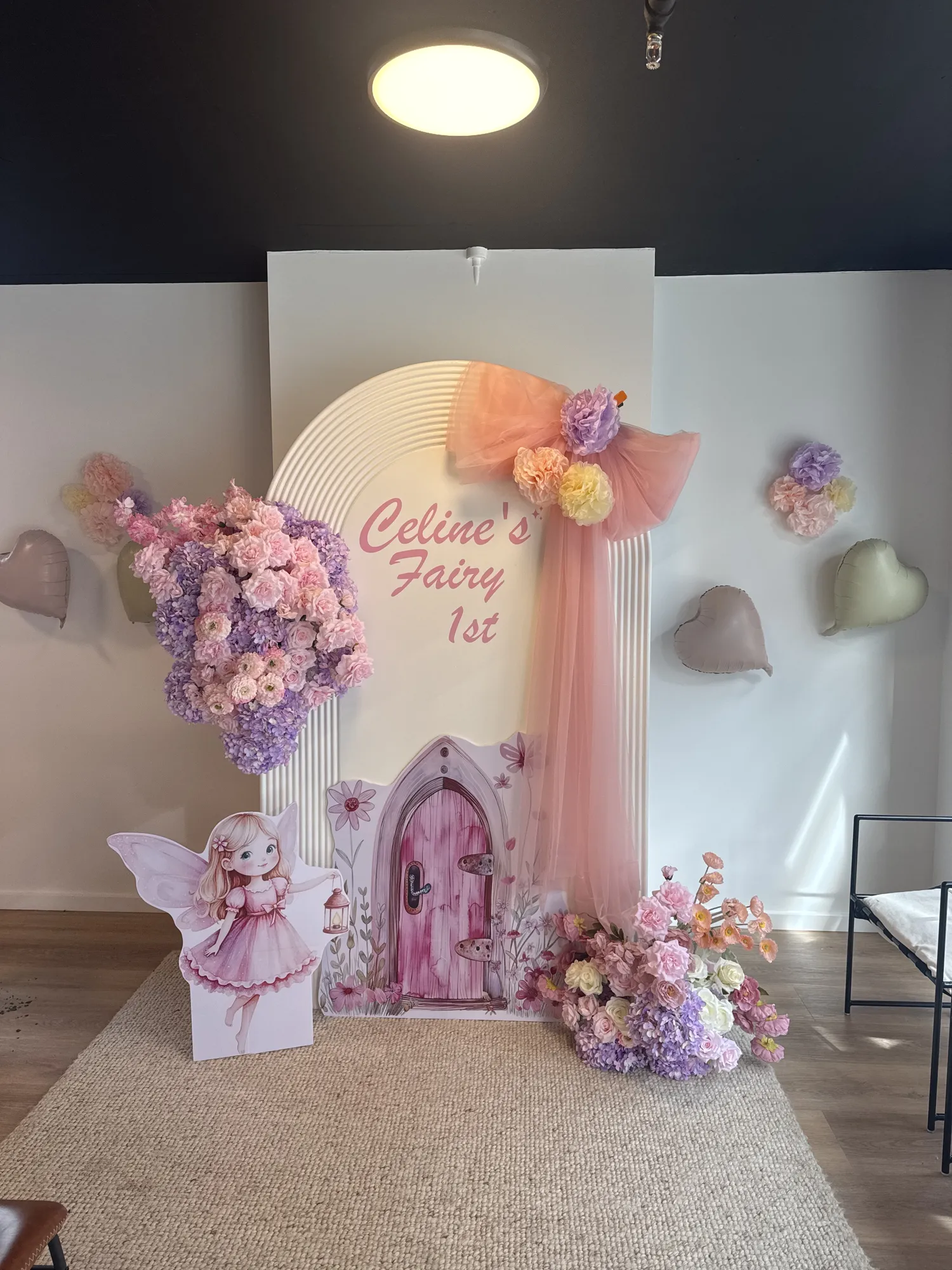 A fairy backdrop in pink and white, with butterfly wings, a marquee 1, a small neon sign, and a butterfly cake on a glass stand.