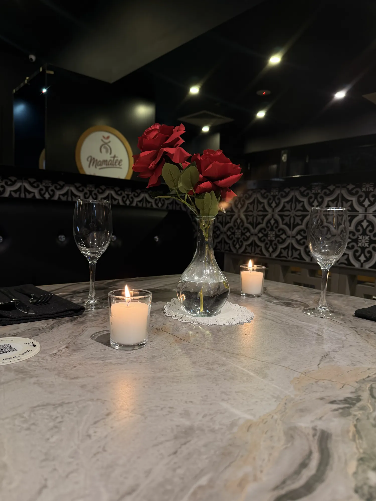 A red carpet leading to a white backdrop with a pink neon sign reading Mamatee, white flowers, and clear plinths.